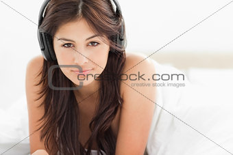 Woman with headphones on, lying down while smiling slightly unde