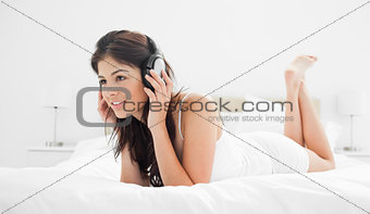 Woman lying on her bed with headphones on, listening to music wh