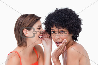 Teenage girl whispering a secret to a surprised friend