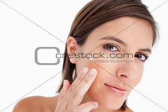 Young woman tilting her head while putting some cream on her fac