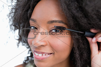 Young smiling woman applying mascara on her eyelashes