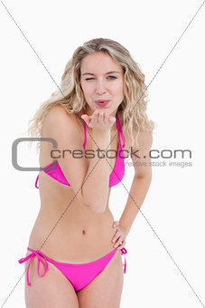 Young blonde woman blinking an eye while sending an air kiss