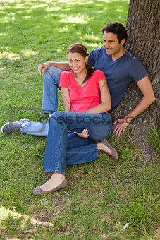 Two friends sitting together against a tree