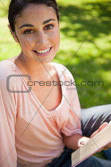 Woman looking ahead as she reads a book while sitting down 