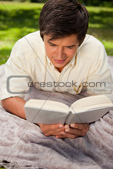 Man reading book while he lies on a blanket