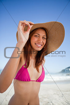 Young smiling woman holding her hat brim while wearing a pink sw