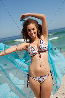 Young smiling woman walking on the beach while holding a blue sa