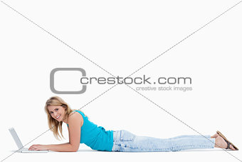 A woman smiling at the camera is lying on the ground typing on h