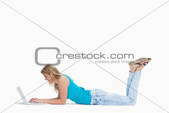 A woman lying on the floor with her legs up is typing on her lap