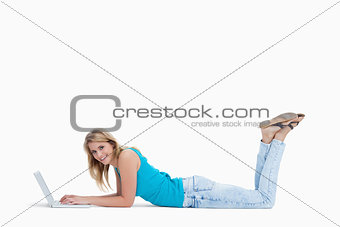 A smiling woman lying on the floor with her laptop 