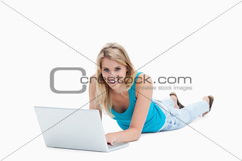 A smiling woman is lying on the floor with a laptop in front of 