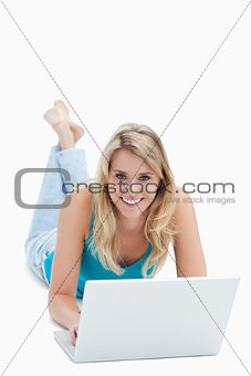 A woman with a laptop is lying on the ground and smiling at the 