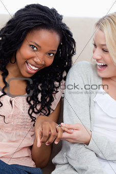 A woman  smiling at the camera is showing her friend her wedding