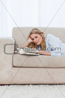 A woman lying on a couch resting her head on her hand is reading