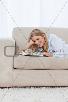 A smiling woman lying on a couch resting her head on her hand is