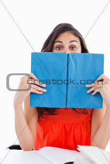 Portrait of a student hiding behind a blue book