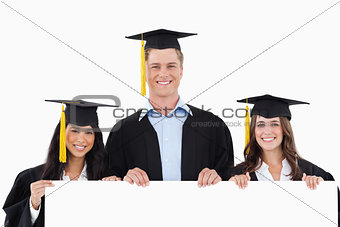 Three students having graduated holding a blank poster