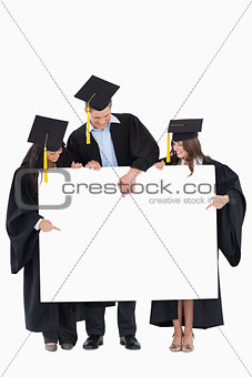 Three graduates pointing to the blank sign