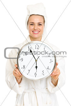 Smiling young woman in bathrobe holding clock