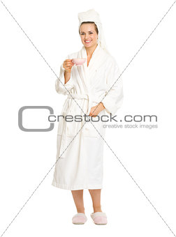 Full length portrait of smiling young woman in bathrobe with cup