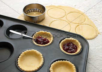 Cutting and filling pastry shapes to make jam tarts 