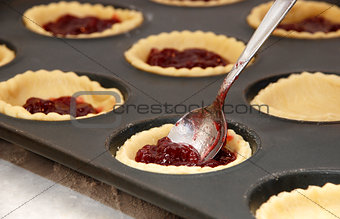 Closeup of jam tarts being filled with a teaspoon