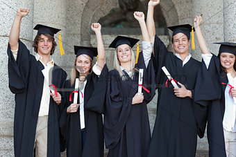 Smiling graduates posing while raising arms