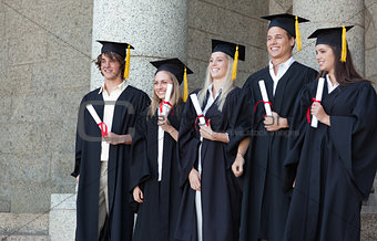 Smiling graduates posing while holding their diploma