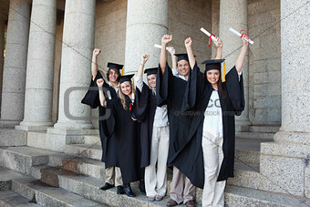 Five happy graduates posing the arms raised