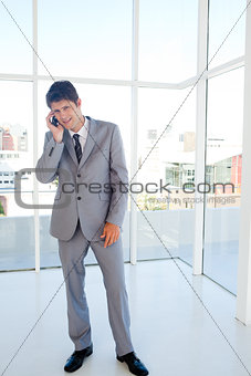 Smiling businessman making a call while leaning his head to the 