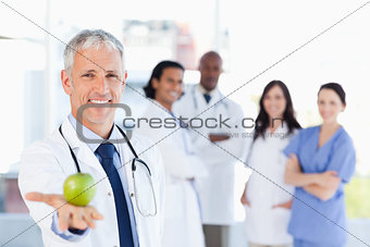 Mature doctor holding an apple while his medical team is looking