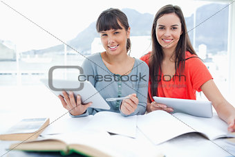 A pair of smiling girls doing work with tablets as they look int