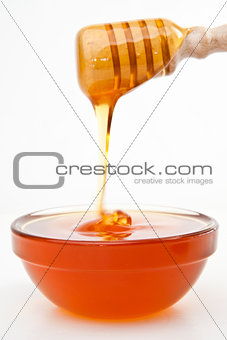 Honey on a honey dipper dropping in a bowl