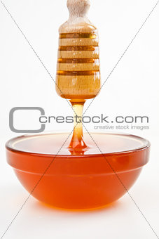 Thin honey trickle dropping in full honey bowl