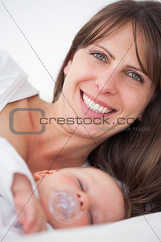 Smiling brunette woman lying while her baby is sleeping