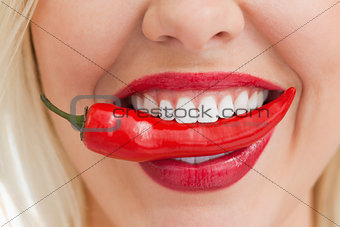 Happy blonde woman holding a chili with her mouth