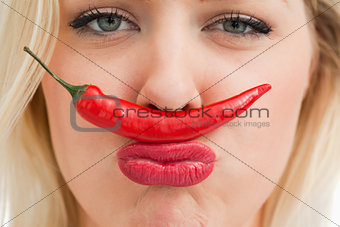 Cheerful woman placing a chili between her nose and her mouth