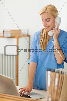Blonde nurse calling while using a laptop