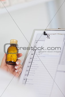 Hand holding bottle of drugs next to a clipboard