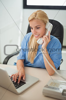 Nurse typing on a laptop while holding a phone
