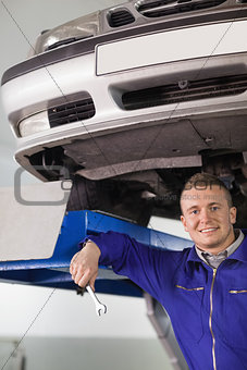 Smiling mechanic holding a spanner below a car