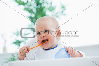 Baby holding a spoon while putting it in his mouth
