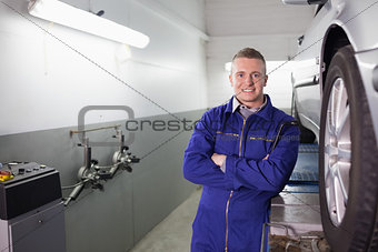 Front view of a mechanic with arms crossed next to a car