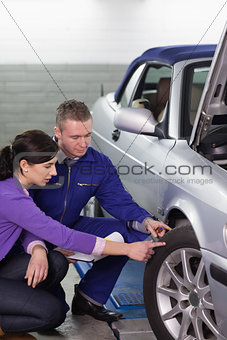 Mechanic touching the car wheel next to a woman