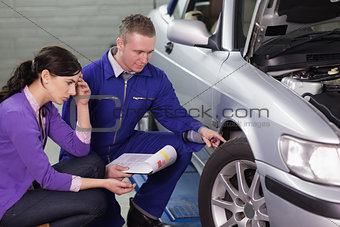 Mechanic looking at the car wheel next to a client
