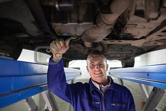 Smiling mechanic looking at camera while repairing a car