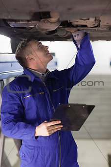 Mechanic looking at the below of a car while holding a clipboard