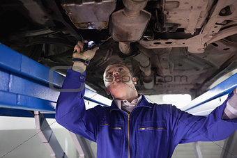 Mechanic looking the below of a car while holding a flashlight