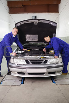 Mechanics smiling while leaning on a car