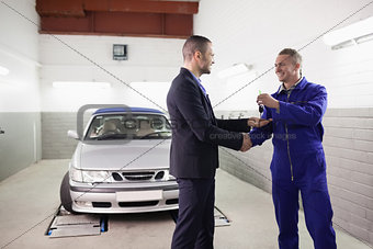 Mechanic giving car key while shaking hand to a client